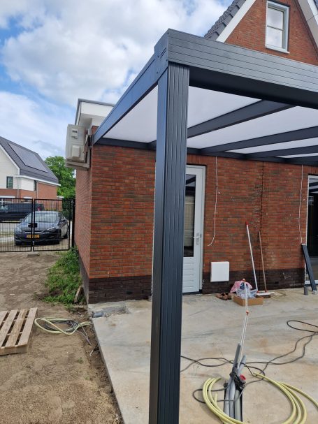 Zijaanzicht van een recent gebouwde pergola naast een bakstenen woning.